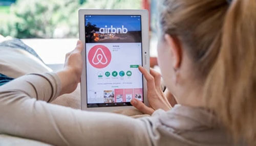 Airbnb program - tycoonstory | tycoonstory media Person using a tablet to browse the airbnb app interface at home - making money on airbnb