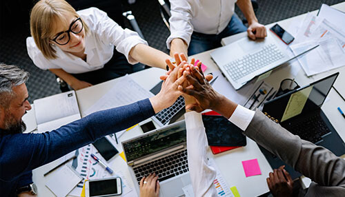 Building a team A team of professionals engaging in a high-five around a table, symbolizing collaboration and teamwork as part of effective staffing strategies