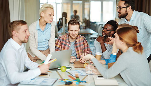 Collaborate A young woman sitting at a desk in a bright room, focused on writing in a notebook with a laptop open beside her. The setting illustrates the dedicated research and planning involved in building a strong financial or professional portfolio.