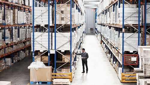 Costs involved in running a complete auditing program inventory A warehouse employee inspecting inventory shelves, ensuring items are properly stored and organized.