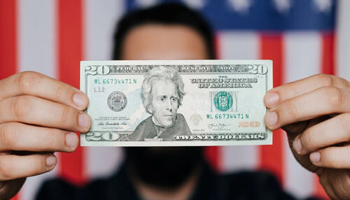 Follow up on pledge - tycoonstory | tycoonstory media Man holding a us dollar bill in front of an american flag, symbolizing us debt-forgiveness and financial policies.