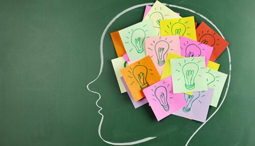 Memory skills Creative brainstorming concept with colorful sticky notes shaped like lightbulbs inside head outline on green chalkboard background.