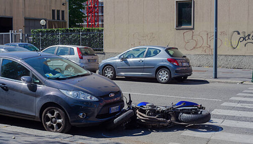 Speed is not the main cause of fatal bike accidents in the us A real-life image of a motorcycle crash, with a fallen motorcycle next to a parked car, capturing the aftermath of the collision on a city street.