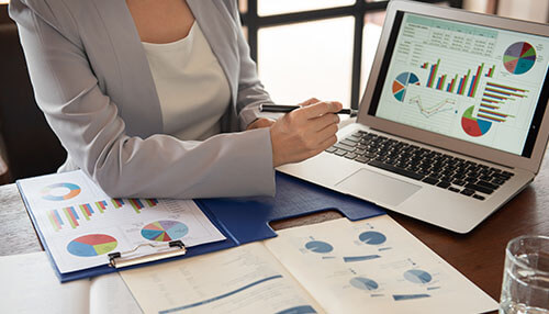 Steps to perform a competitor analysis Professional reviewing competition data on a laptop and papers, highlighting the analysis of the competition using pie charts and bar graphs.