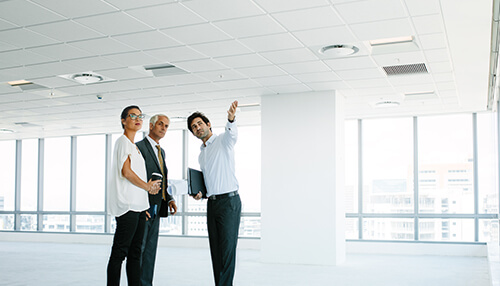 Tips to follow before signing commercial lease for office spaces - tycoonstory | tycoonstory media A business owner and two colleagues inspecting an empty commercial space, discussing potential space leasing opportunities.