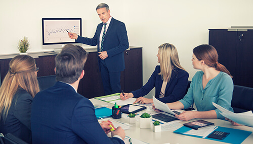 What are the marketing conferences A marketing conference presentation where a speaker is explaining marketing trends, with the audience following along with printed materials and digital charts.