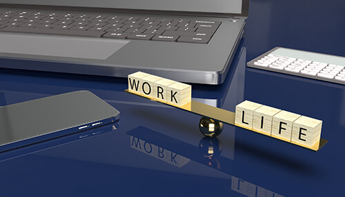 Work-life balance Landlord balancing work and life responsibilities, illustrated by a scale with “work” and “life” blocks placed beside a laptop on a desk.