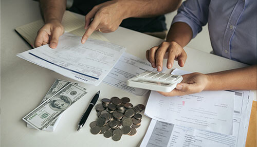 Always know how much money you have Two individuals discussing business finances while reviewing documents, with money, coins, and a calculator on the table