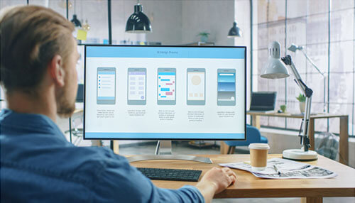 Designing screens and ui elements A designer working on ui design, reviewing mobile app interface mockups on a large monitor to create an engaging user experience.