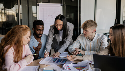 Enhance the culture within your organisation - tycoonstory | tycoonstory media Team collaborating in a meeting, analyzing charts and data together to strengthen problem-solving and critical thinking skills in a professional work environment.