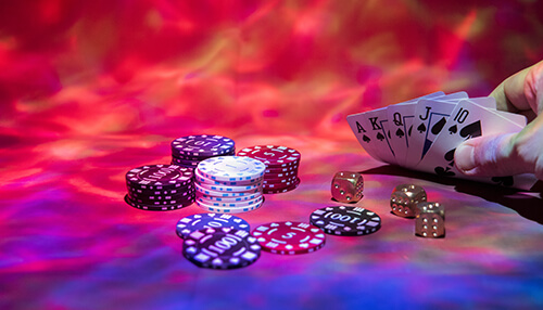 Gambling on social media A hand holding a set of playing cards next to a pile of poker chips and dice, symbolizing a casino or gambling scene.