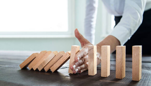 Limited risks Business professional stopping a row of falling wooden blocks, representing risk management and the careful balance in strategic alliances.