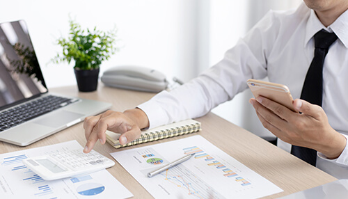 Prepare a narrative budget Budget analysis at office desk with financial charts, notebook, and smartphone used for tracking expenses