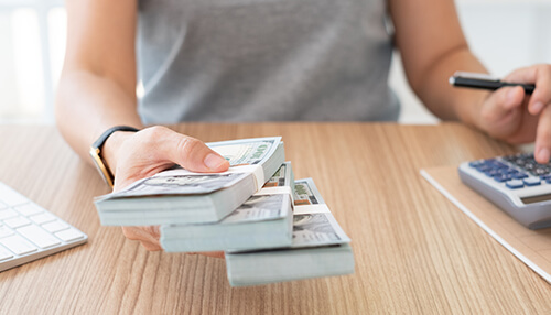 Startup business loans A person holding stacks of cash while calculating finances, symbolizing startup business loans in singapore.