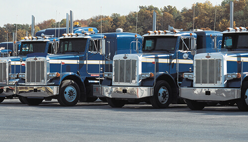 Tips to consider before semi trailer leasing - tycoonstory | tycoonstory media A row of blue semi-trucks parked in a lot, symbolizing the importance of insuring commercial vehicles with liberty mutual car insurance.