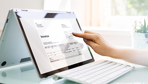 What is a proforma invoice A hand pointing to a digital invoice on a tablet screen next to a keyboard, representing digital processing of proforma invoice and account sales.