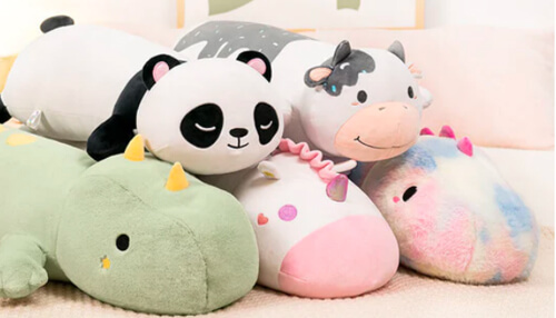 Plush toy - tycoonstory | tycoonstory media Soft plush toys like panda, cow, unicorn, and dinosaur arranged on a bed.