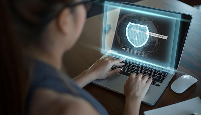 A strong password is essential A woman working on a laptop displaying a holographic shield interface representing cyber security protection.