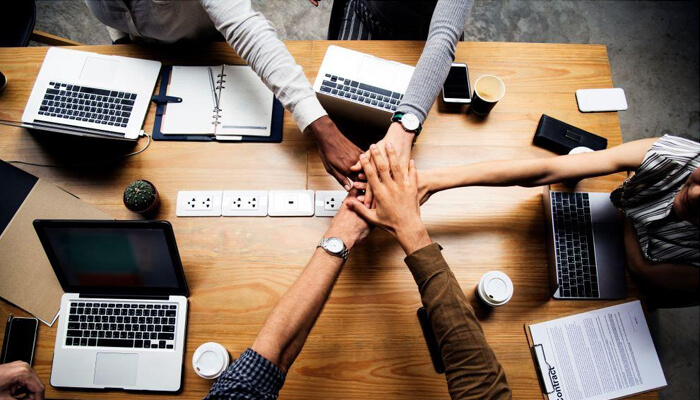 How can outsource seo help your business Outsource seo services: team members collaborating and joining hands, symbolizing teamwork and the importance of outsourcing seo services for business growth.