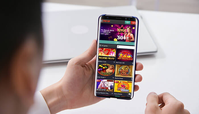 Pin up casino login to your personal account Person holding a smartphone showing the pin-up mobile app with a selection of online casino games and a bonus offer.