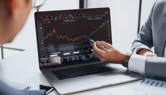 Trader funding Earn2trade platform shown on a laptop with financial charts, as two professionals analyze market data and trends for trading decisions