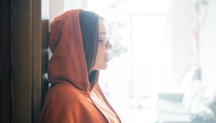 Vaping and morale Person in an orange hoodie exhaling smoke from a vape, highlighting the growing popularity of vaping.