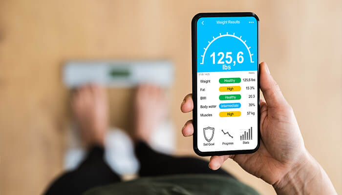 Alternative measures of progress Close-up of a smartphone showing a digital weight tracking app with detailed health metrics on top of a weight scale.