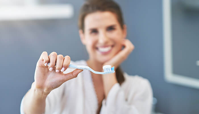 Caring for your teeth beyond toothpaste Smiling woman holding a toothbrush with toothpaste, demonstrating proper dental care and oral hygiene.