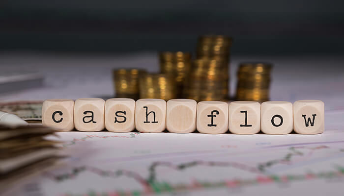 Cash flow management Cash flow spelled with wooden blocks and stacked coins in the background, illustrating improved financial management and profitability supported by document generation software.