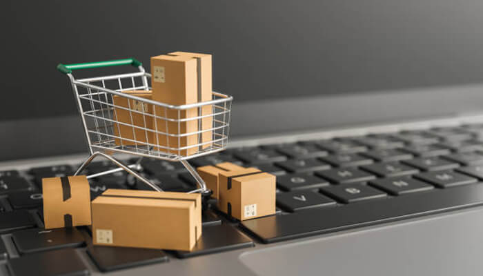Drop shipping - tycoonstory | tycoonstory media A small shopping cart filled with cardboard boxes placed on a laptop keyboard, symbolizing e-commerce and start-up online sales.