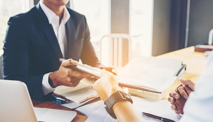 Establish a strong business plan Business owner submitting documents to a lender during a business loan application meeting.