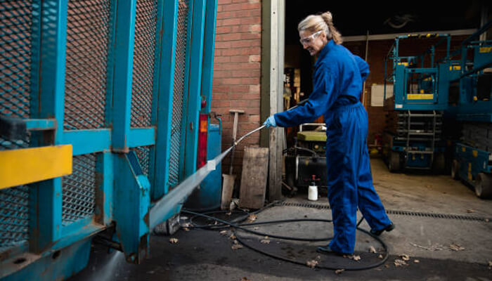 Quickly revitalise your business premises Briggs industrial worker pressure washing metal equipment inside a workshop.