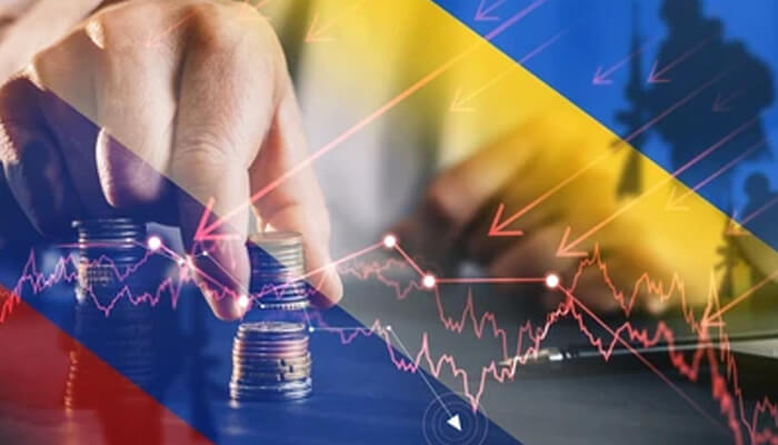 Ukraine gdp fell greatly during the russia ukraine war Hand stacking coins overlaid with falling market charts and the ukraine flag, symbolizing economic impact of the conflict.