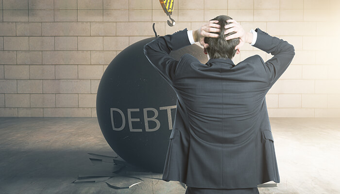 Taking on too much debt Man in a suit holding his head while facing a large debt ball, illustrating financial mistakes related to taking on too much debt and poor financial decision-making.