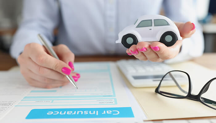 The insurance company - tycoonstory | tycoonstory media Woman holding a toy car while reviewing car insurance documents, illustrating how claims are handled when a driver is in partial fault.