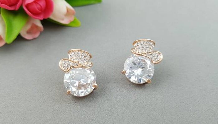 The ideal union of studs and stones Rose gold stud earrings with large clear gemstones and intricate diamond-like accents, offering a stylish and elegant design