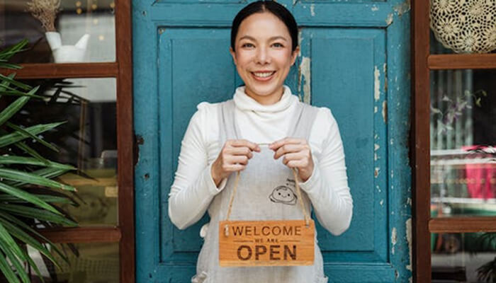 Traditional small business loans A small business owner holding an'Open' sign outside her shop, symbolizing the success of funding a small business and welcoming customers
