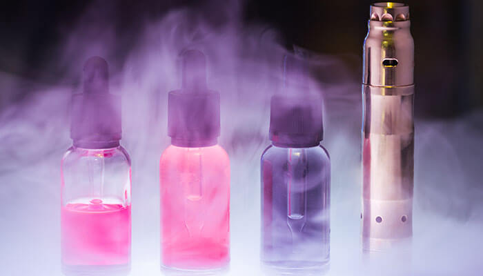 Bottled e-liquid - tycoonstory | tycoonstory media Vape juices in colorful bottles, surrounded by smoke, displayed in a vape shop, highlighting the variety of flavors available.