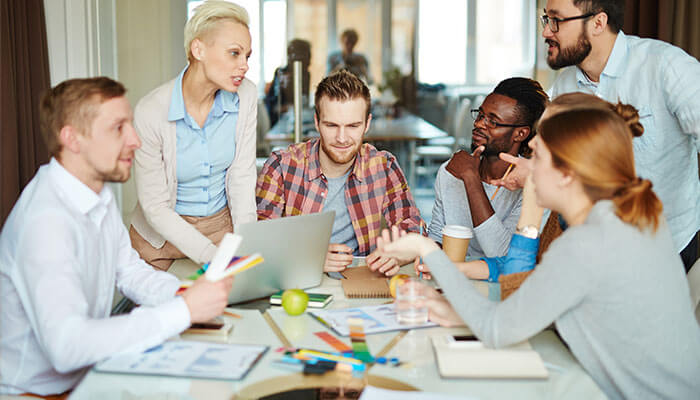 Enhanced collaboration A group of professionals engaged in a creative discussion around a table, representing collaboration and teamwork facilitated by idea management software to overcome organizational barriers.