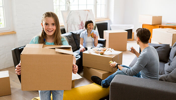 Moving checklist A family is pictured in a living room, with moving boxes scattered around. A child carries a box as part of the moving checklist process, preparing for a move to a new home.