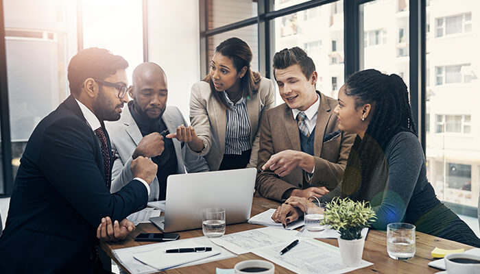 Promotes open communication Business team gathered around a laptop in a meeting, discussing tasks despite fatigue and pressure, illustrating presenteeism and reduced workplace productivity.