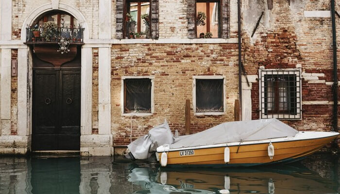 The normal threshold for the venice canals A canal in venice with a yellow boat docked by a brick building featuring large windows and a wooden door, capturing the charm of venice's waterways.