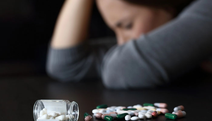 The psychological effects of heroin addiction Image showing spilled pills with a person in the background, representing the psychological effects of heroin addiction and the need for heroin rehab and recovery support.