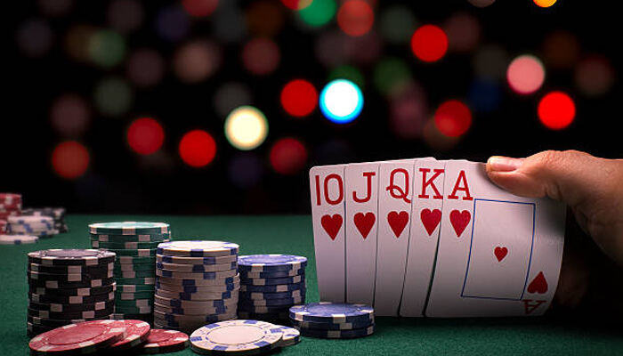 Types of poker A player reveals a winning poker hand of a royal flush in hearts, surrounded by colorful casino chips on a green table with blurred lights in the background.