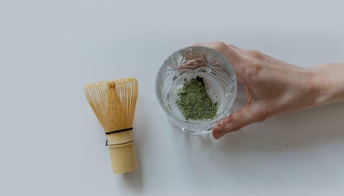 What is an mit 45 shot Matcha powder and a glass of water on a white surface, representing preparation steps linked with mit45 wellness routines.
