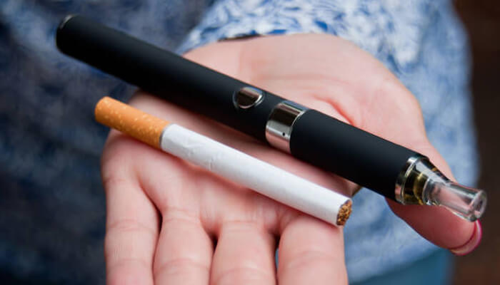 Why vaping is less dangerous than smoking A hand holding a black vaping device next to a traditional cigarette, comparing smoking and vaping.