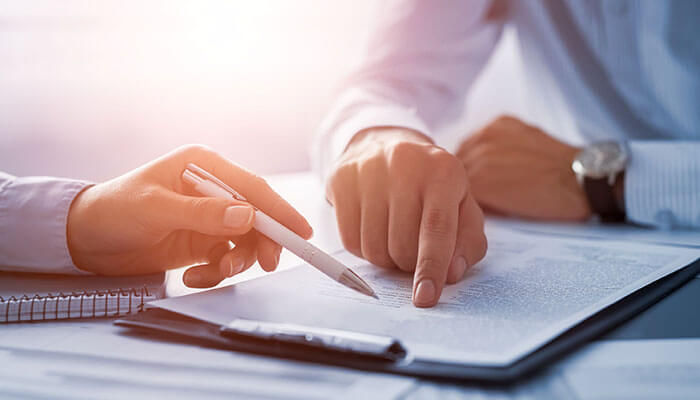 Do your homework Two people review a document, one pointing while the other holds a pen, suggesting a commercial insurance or legal discussion.