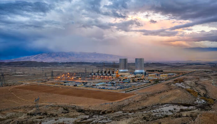 Iran Aerial view of a nuclear power plant in iran with cooling towers, surrounded by desert terrain and mountains in the background.