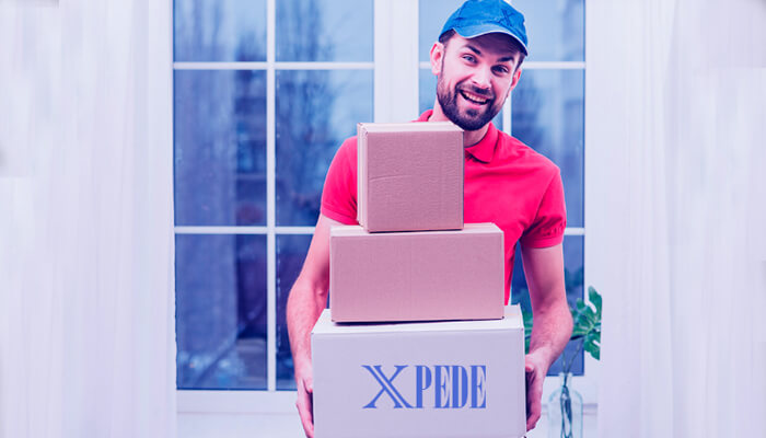On demand delivery service A smiling delivery worker holding stacked packages with xpede branding inside a bright home setting.