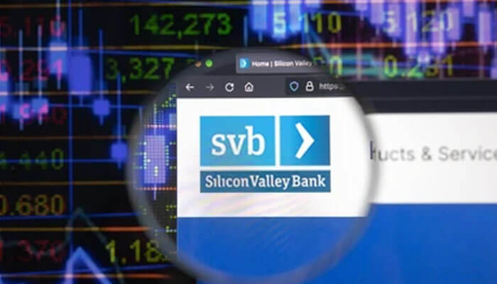 Svb - tycoonstory | tycoonstory media A conceptual digital image showing the silicon valley bank logo and website viewed through a circular magnifying glass effect. The background consists of a dark, blurry stock market data screen with glowing green and red numbers and blue bar charts, suggesting a focus on financial analysis or news regarding the bank.